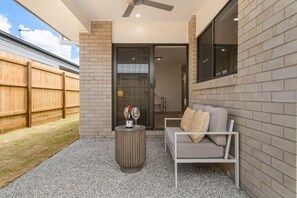 An outdoor patio area with a sofa, a round table, and a bottle of wine.