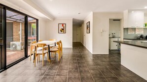 Une cuisine moderne avec des carreaux de couleur sombre, un coin repas avec des chaises en bois et une porte vitrée donnant sur l’extérieur.