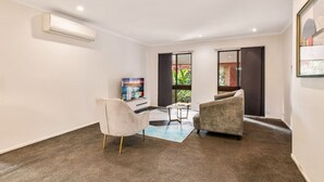 Un salon moderne doté d’un téléviseur à écran plat, de deux fauteuils, d’une table basse et d’une grande fenêtre donnant sur un paysage verdoyant.