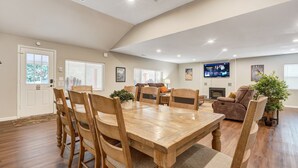 A spacious living room with a wooden dining table and chairs, a comfortable sofa, and a television mounted on the wall. - Mountain Retreat (Cascade)
