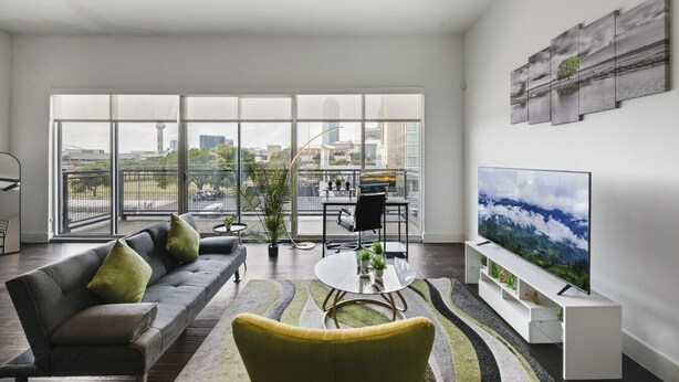 A spacious living room with a large window, a sofa, a coffee table, and a TV. - City View 1BR I Gym I Free Parking I Workspace (Dallas)
