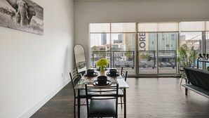 A modern dining area with a table set for two, a large window with a city view, and a black sofa in the background. - City View 1BR I Gym I Free Parking I Workspace (Dallas)