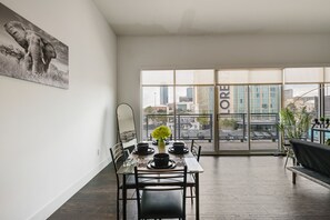 A modern dining area with a table set for two, a large window with a city view, and a black sofa in the background. - City View 1BR I Gym I Free Parking I Workspace (Dallas)