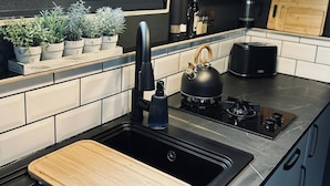 Una cocina moderna con un lavamanos negro, estufa de acero inoxidable y tabla de cortar de madera.