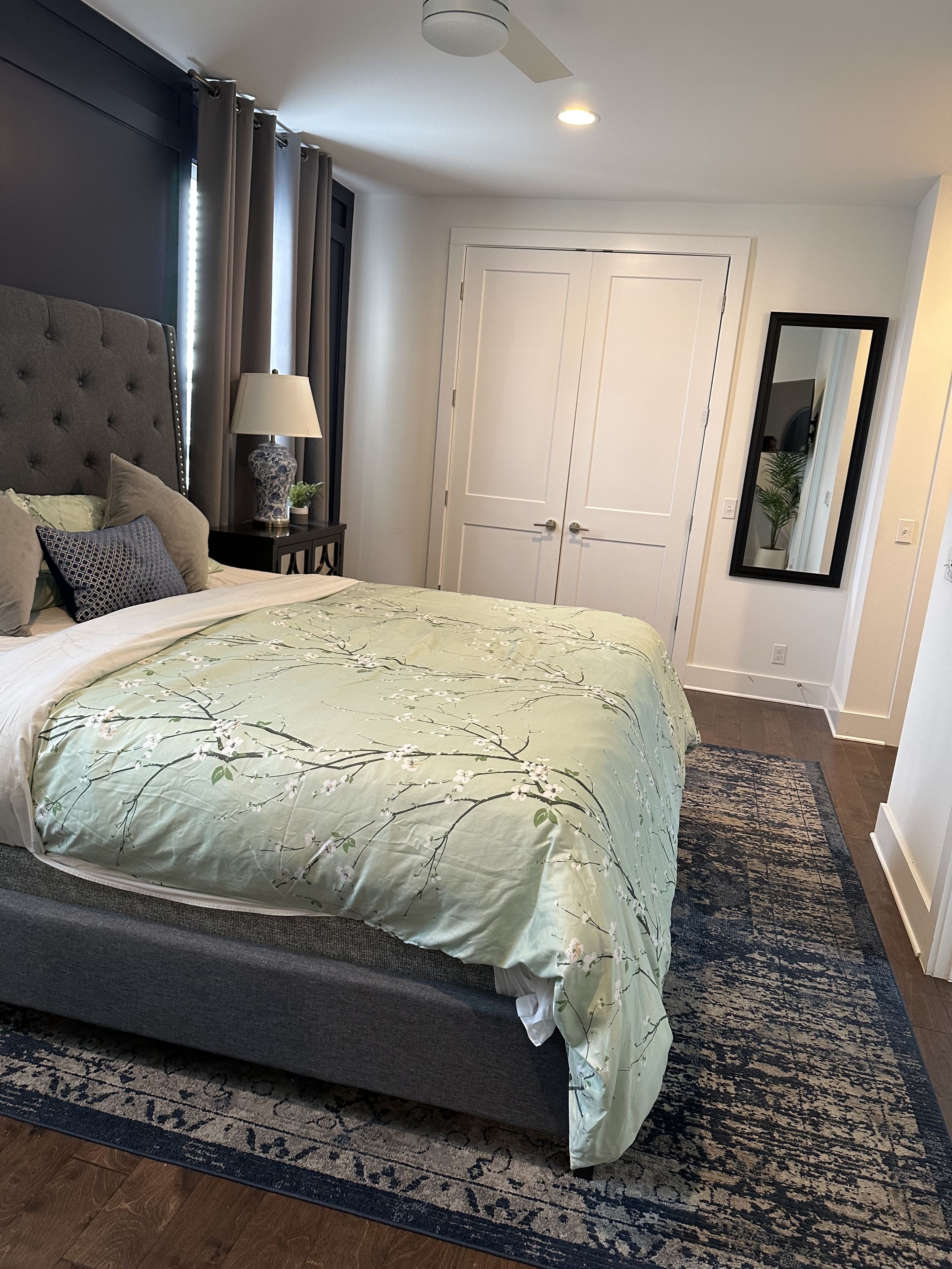Une chambre à coucher avec un grand lit, une table de chevet avec une lampe, un ventilateur de plafond et une porte dotée d’un miroir.