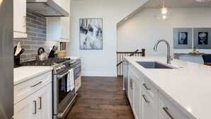 Une cuisine moderne avec des meubles blancs, une cuisinière en acier inoxydable et un grand îlot central doté d’un évier.