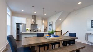 Une cuisine moderne avec des meubles blancs, des appareils en acier inoxydable et une table à manger en bois, assortie de chaises bleues.