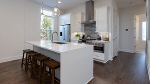 Une cuisine moderne avec des meubles blancs, un grand îlot central doté de tabourets, des appareils en acier inoxydable et un mur de fond en briques.
