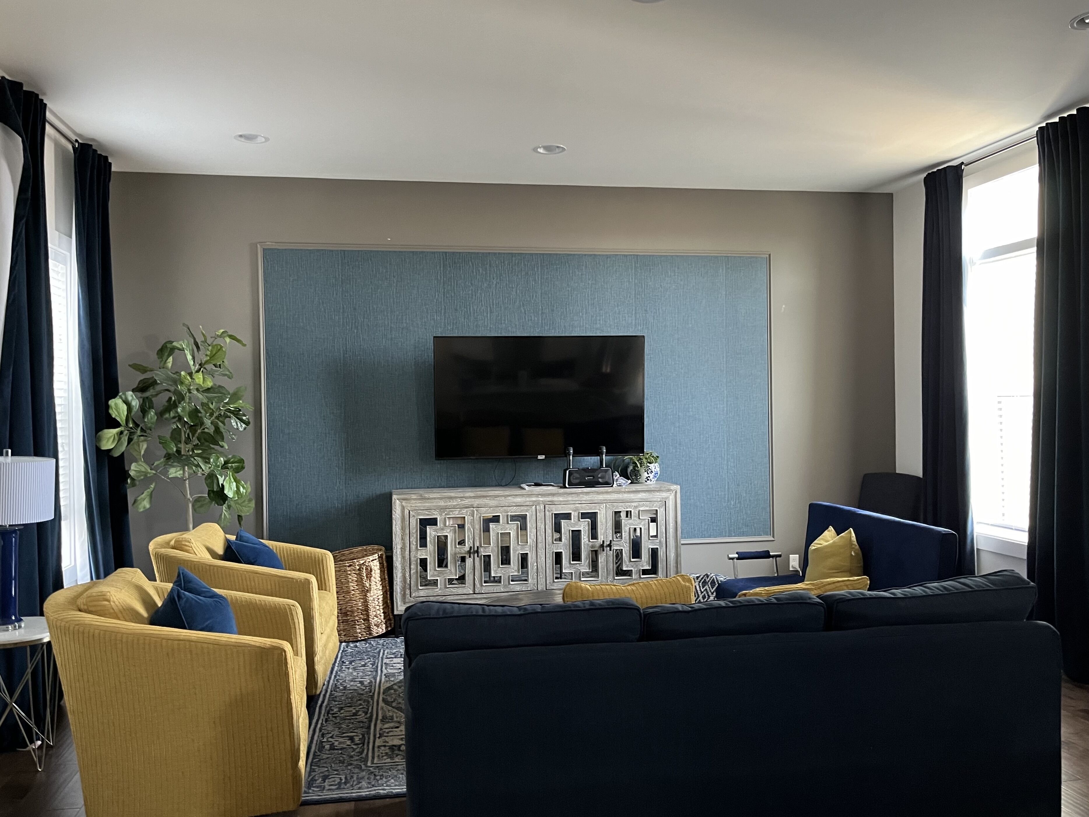 A living room with a large flat-screen TV mounted on a textured wall, a sofa set, a coffee table, and a potted plant.