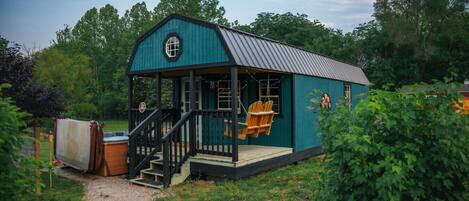 A small, single-story building with a porch and a swing chair.