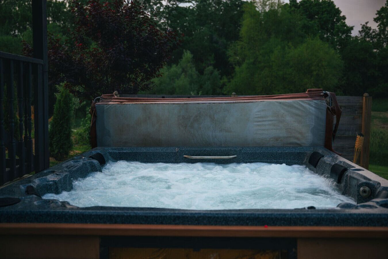 Un jacuzzi con banco de madera y estructura metálica, rodeado de follaje.