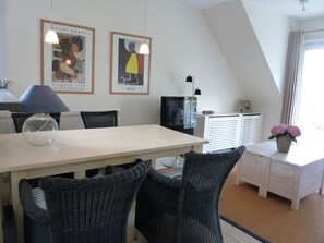 Une pièce moderne comprenant une table à manger, des chaises en osier, un téléviseur et des œuvres d’art accrochées au mur.