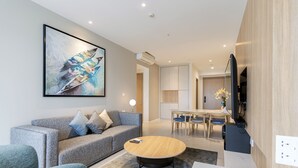 A modern living room with a grey sofa, a round coffee table, and a flat-screen TV mounted on the wall. - Le Places ZENITY Apartment District 1 (Ho Chi Minh City)