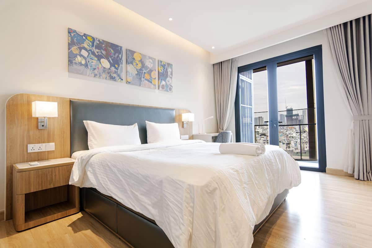 Ein modernes Hotelzimmer mit einem großen Bett, Holz-Nachttischen und Blick auf die Stadt durch das Fenster.