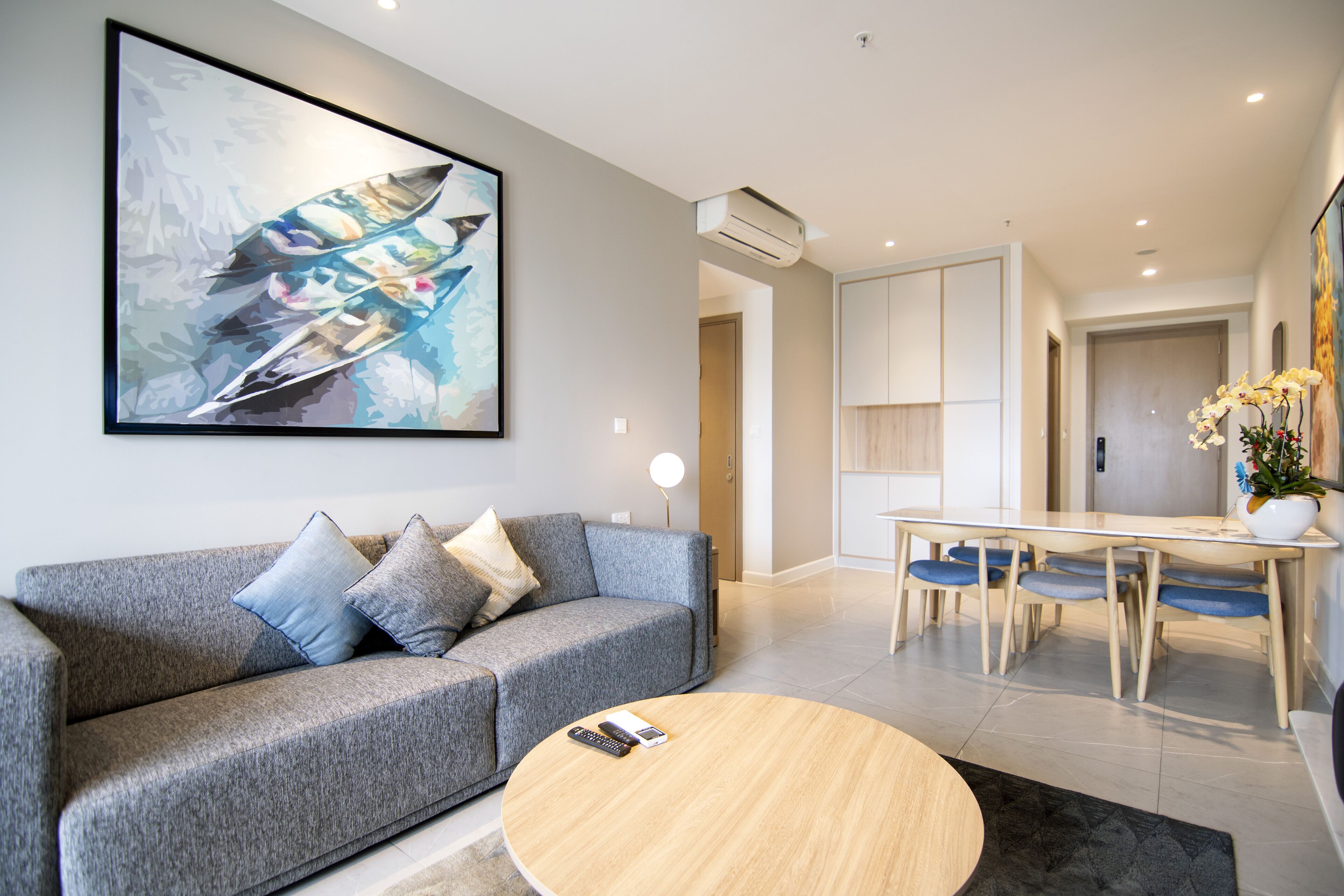 A modern living room with a grey sofa, a round coffee table, and a dining area with a wooden table and chairs.