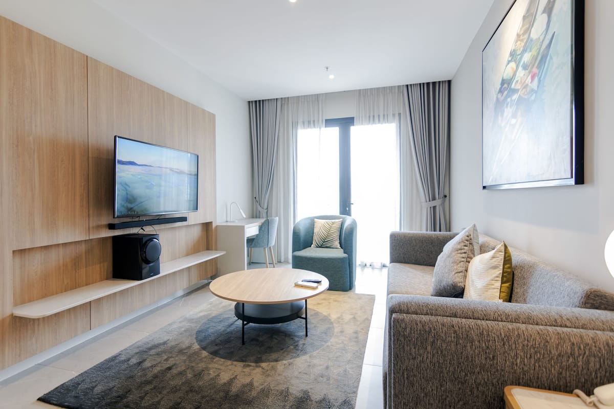 Ein modernes Wohnzimmer mit Flachbildfernseher, rundem Couchtisch, Sofa und Sessel.