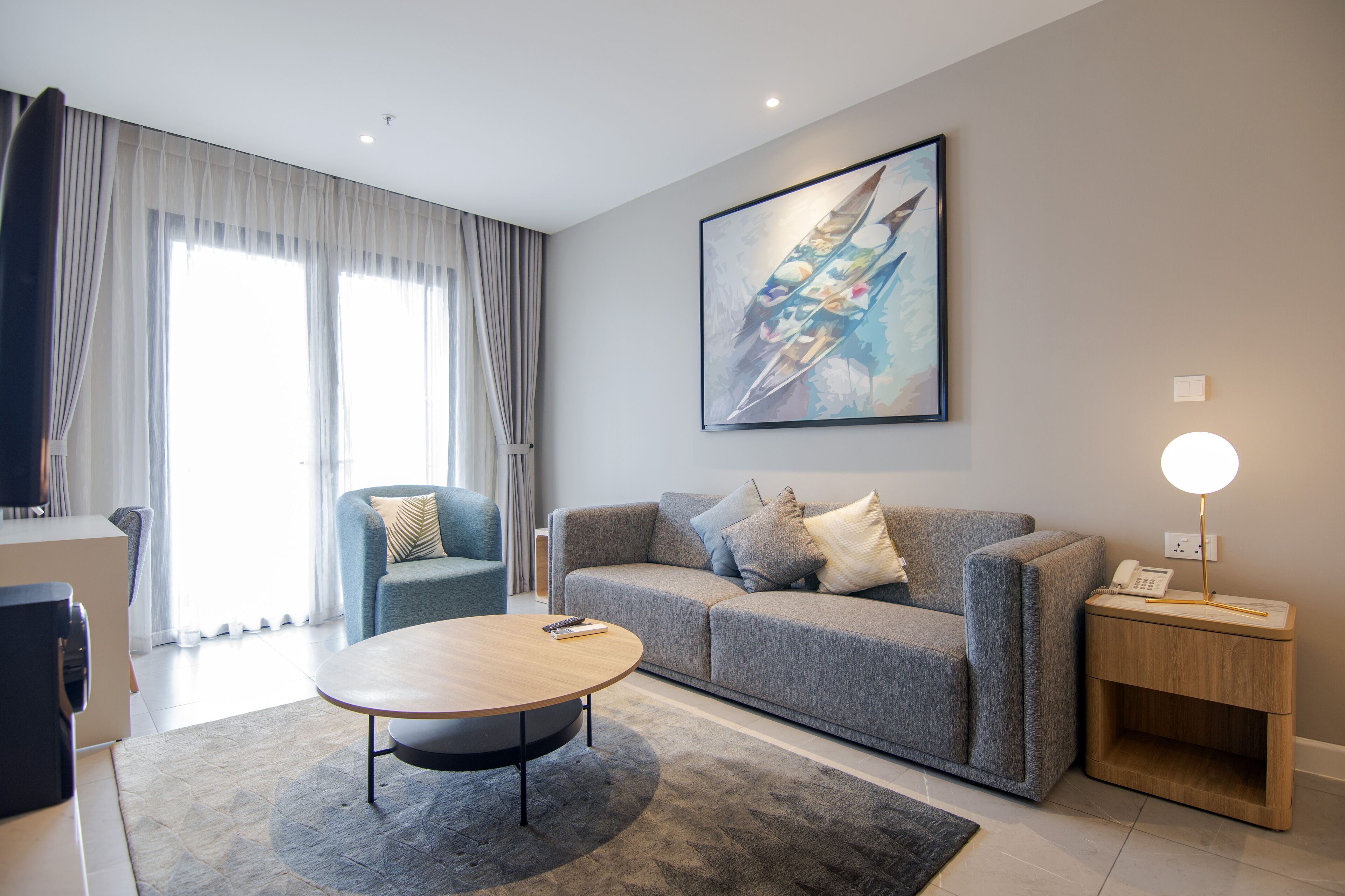 A modern living room with a grey sofa, a round coffee table, and a painting on the wall.