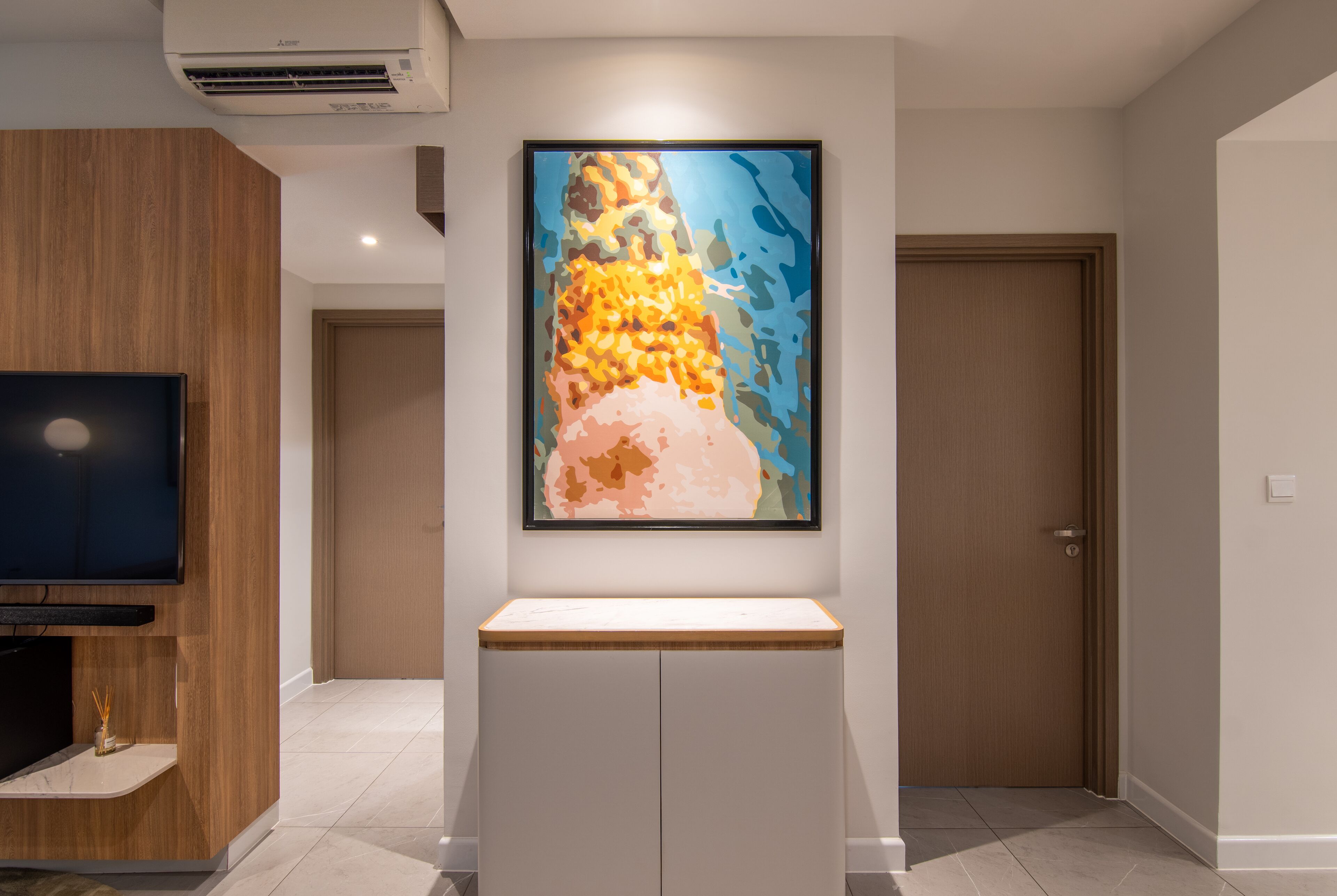A modern living room with a flat-screen TV, a framed abstract painting, and a wooden cabinet.