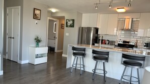 A modern kitchen with a central island, stainless steel appliances, and bar stools. - Amazing Views, DT, Free Parking  (Vancouver)