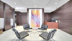 A modern lobby with a reception desk, three black leather chairs, and a large abstract painting on the wall. - Amazing Views, DT, Free Parking  (Vancouver)