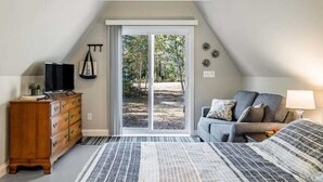 Une chambre à coucher comprenant un lit, une commode, un téléviseur et une porte-fenêtre coulissante donnant sur un balcon.