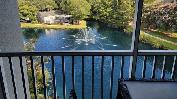 Une vue sur un lac avec une fontaine, entouré d’arbres et d’une maison.