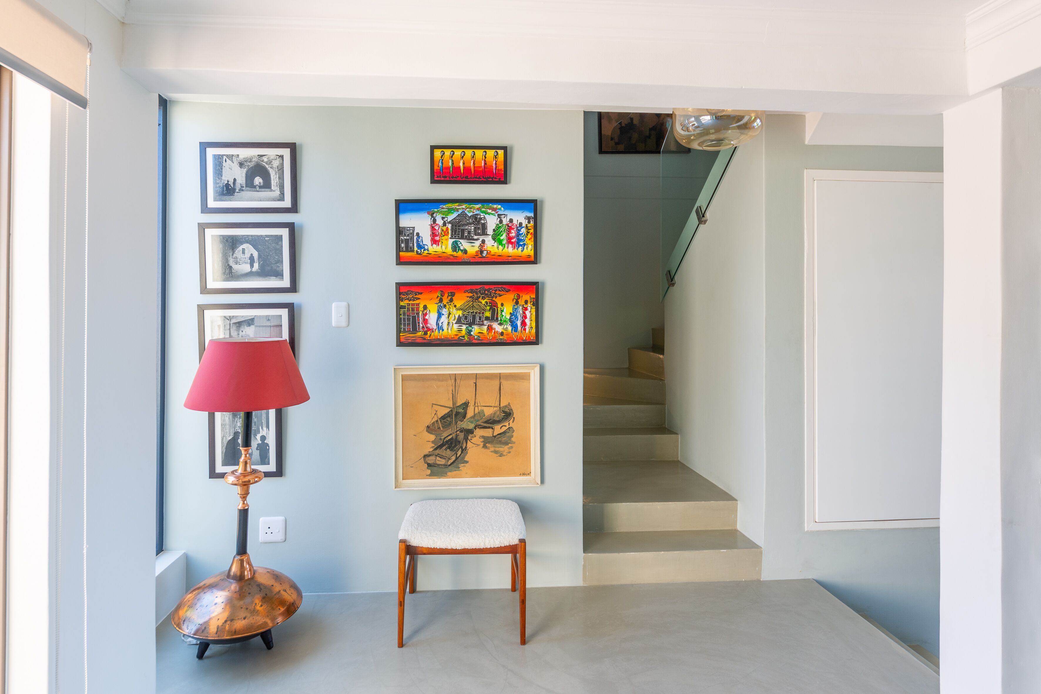 A hallway with a staircase, a red lamp, and a chair.