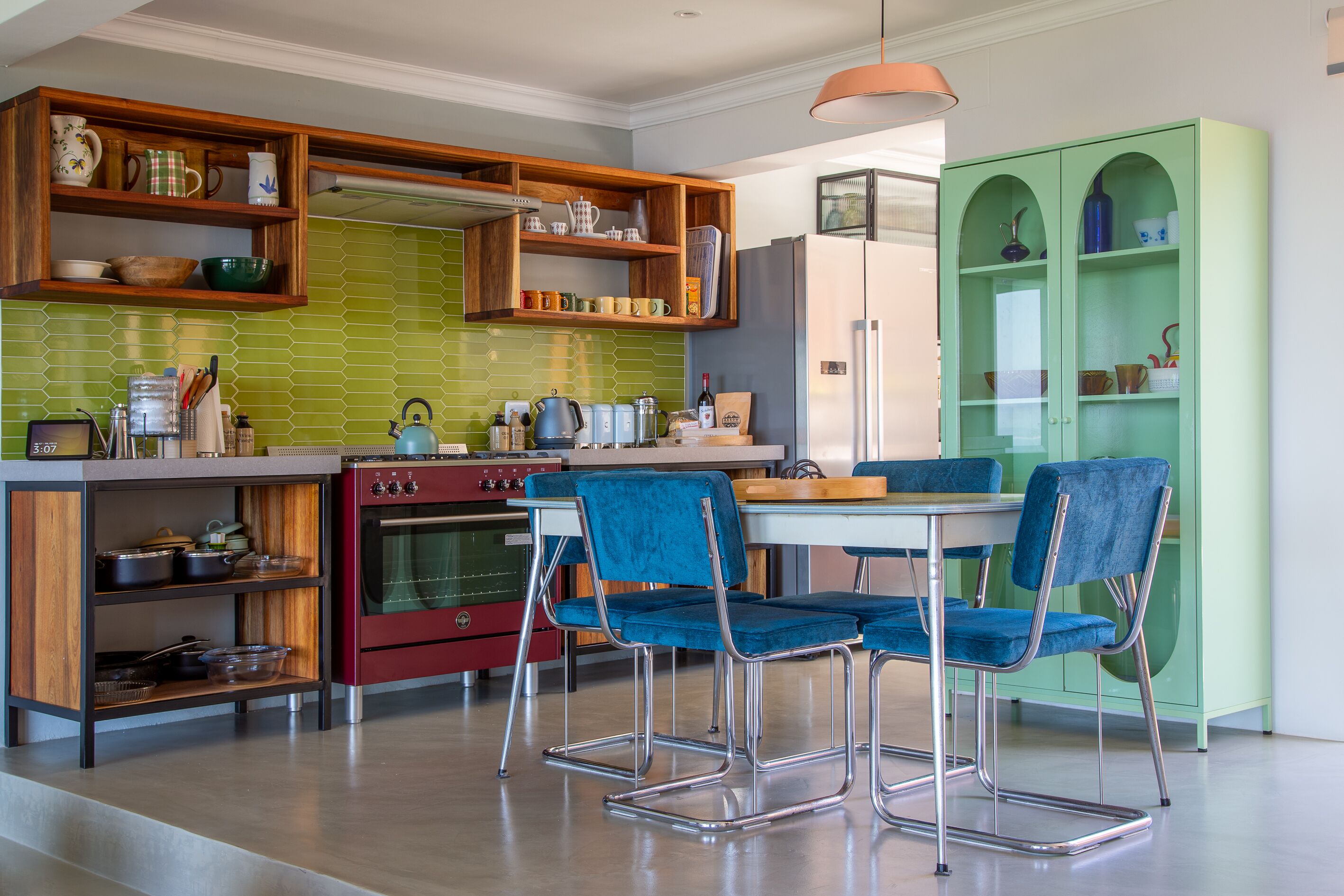 A modern kitchen with wooden shelves, a red oven, and blue chairs.