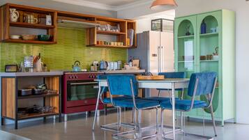 A modern kitchen with wooden shelves, a red oven, and blue chairs.