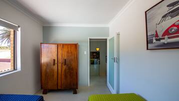 Een slaapkamer met een houten garderobe, een bed met een deken met een blauw en groen patroon, en een lijst met daarop een foto van een oldtimer.