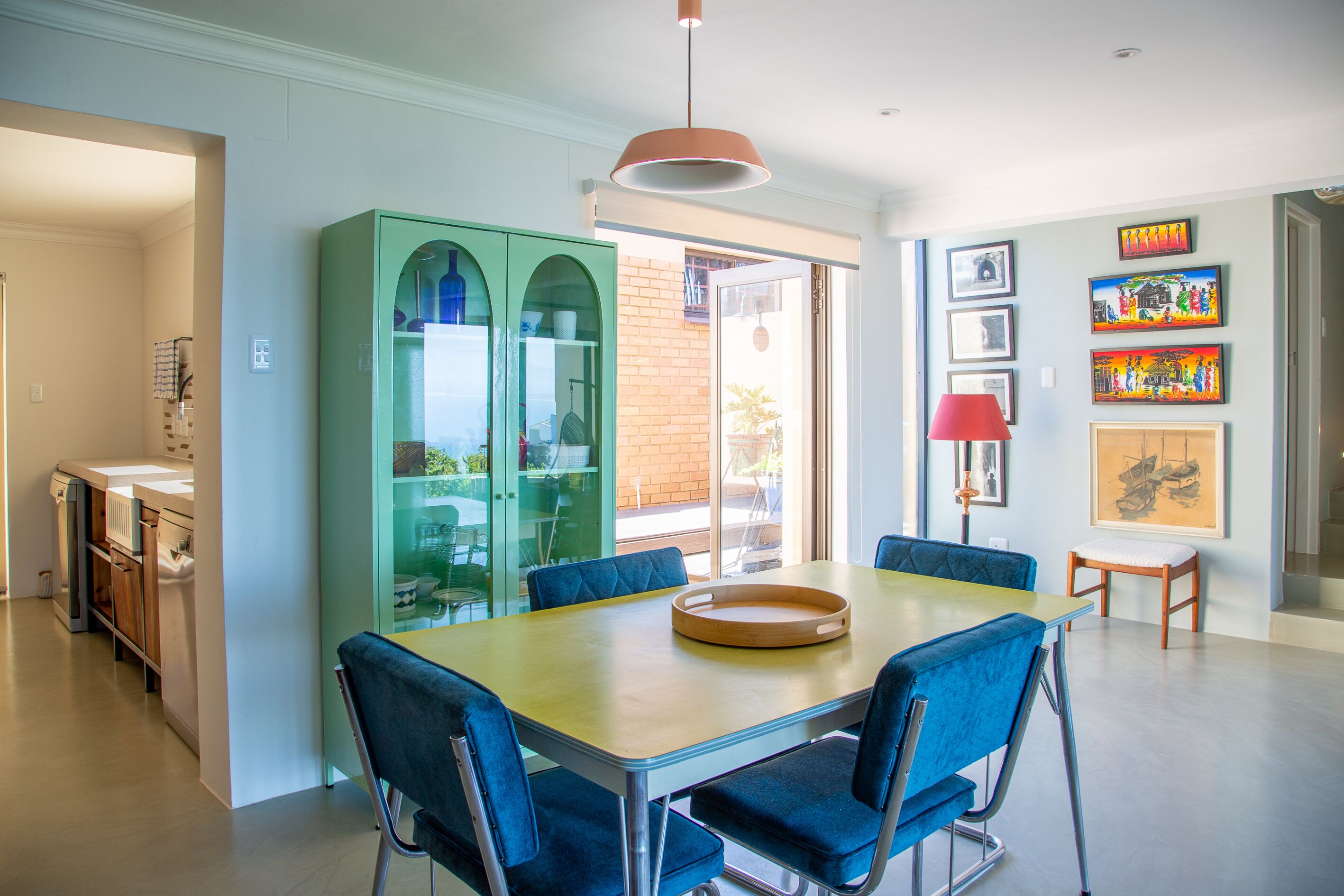 A modern dining area with a wooden table, blue upholstered chairs, and a green cabinet with glass doors.