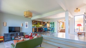 A modern living room with a sofa, coffee table, and TV. There is a kitchen area with a dining table and chairs.