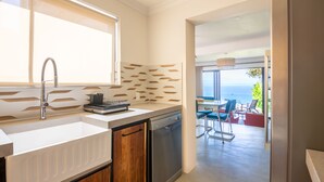A modern kitchen with a large window, a dishwasher, and a dining area with a view of the ocean.