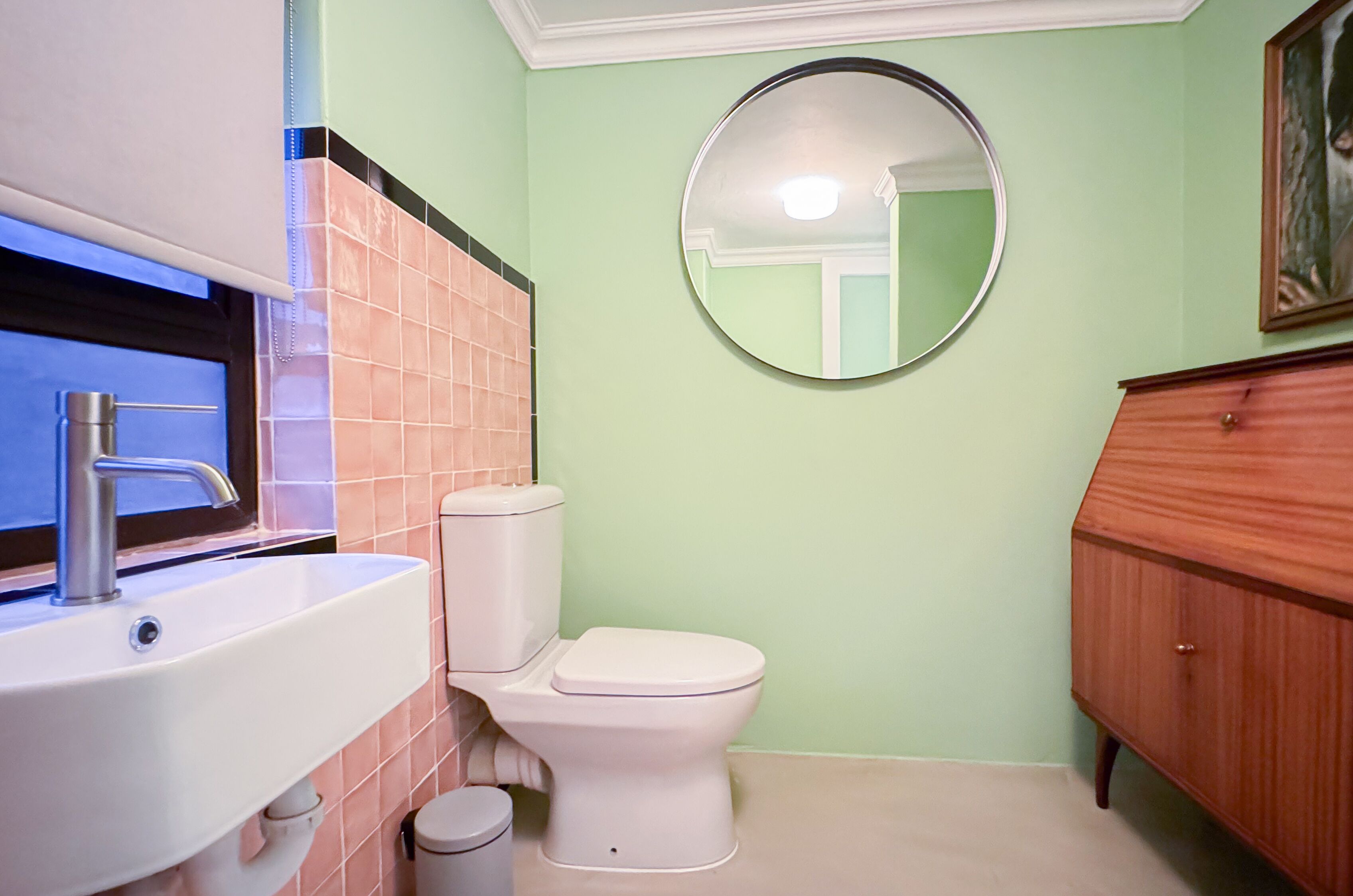 A bathroom with a white sink, toilet, and a round mirror on the wall.