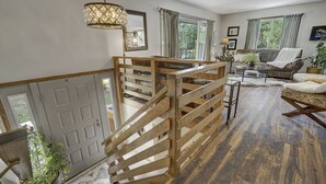 A spacious living area with a wooden staircase, a sofa, a coffee table, and a view of the outdoors. - Sunnywood (Woodland Park)