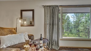 A bedroom with a large window, a bed with a headboard, a bedside table with a bottle and glasses, and a mirror on the wall. - Sunnywood (Woodland Park)