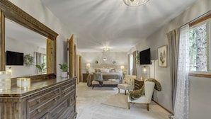 A bedroom with a large bed, a vanity with a mirror, a dresser, and a television mounted on the wall. - Sunnywood (Woodland Park)