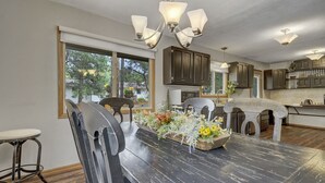 A dining area with a wooden table, chairs, and a floral centerpiece. There are cabinets and a kitchen in the background. - Sunnywood (Woodland Park)