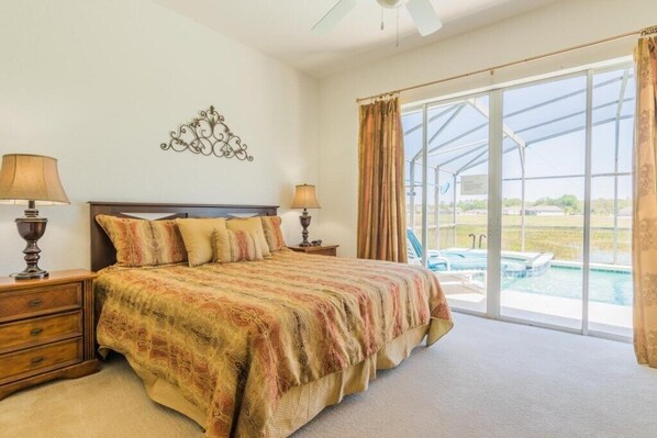 A bedroom with a large bed, two bedside tables with lamps, a decorative wall piece, and a large window with a view of a swimming pool.