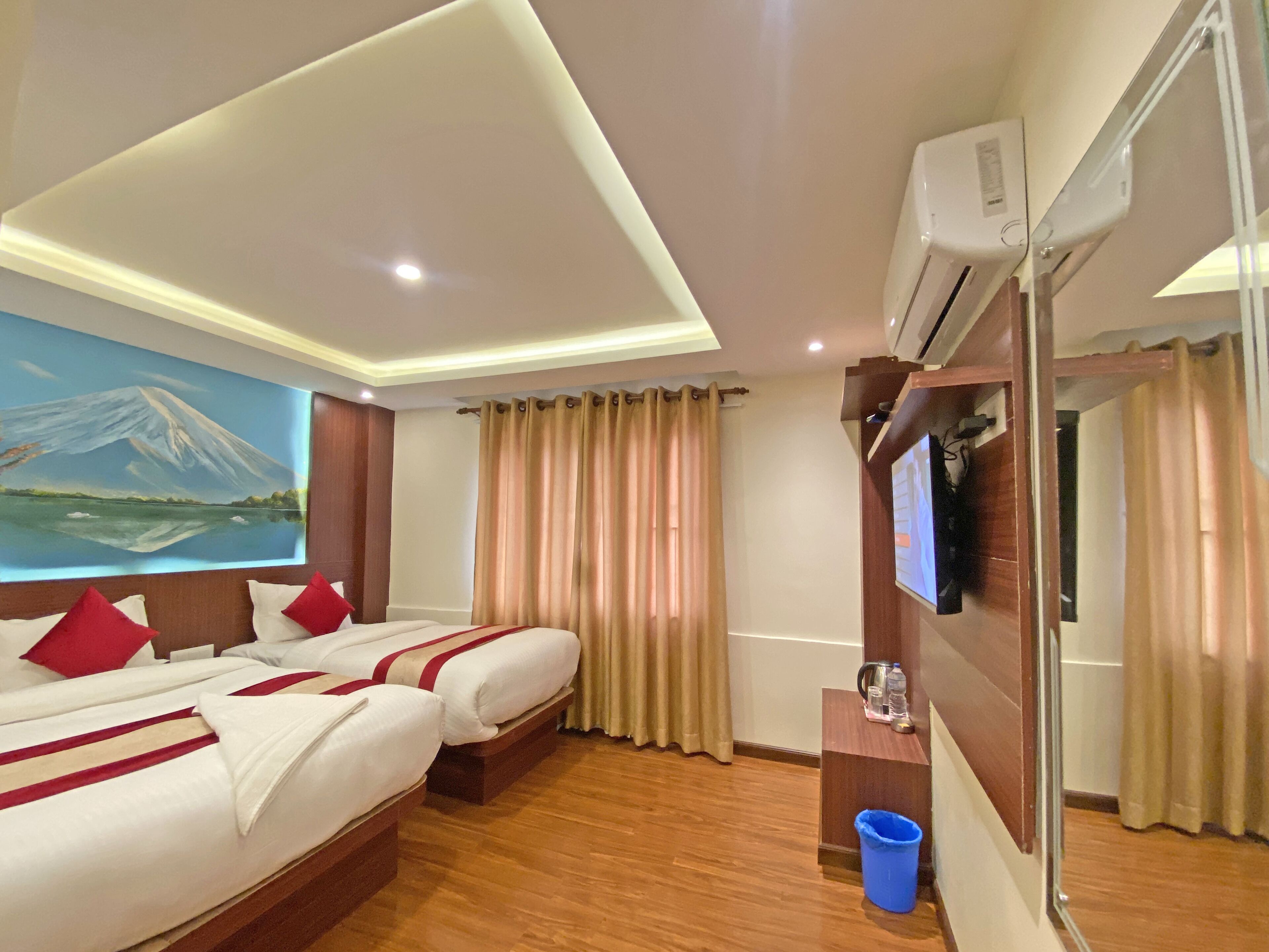 A hotel room with two beds, a painting of a mountain, a TV, and an air conditioning unit.