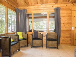 Ein Interieur einer Holzhütte mit Korbmöbeln, großen Fenstern und Blick auf Bäume.