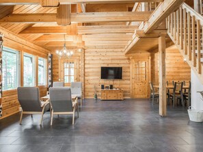 A spacious wooden cabin interior with a dining area, a living room with a TV, and a staircase.