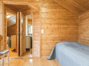 Ein Zimmer in einer Holzhütte mit einem Bett, einem Stuhl und einer Tür zu einem anderen Raum.