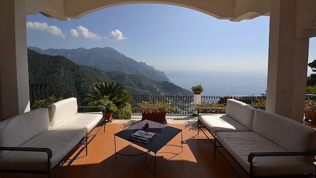 A terrace with two white sofas, a small table, and potted plants.