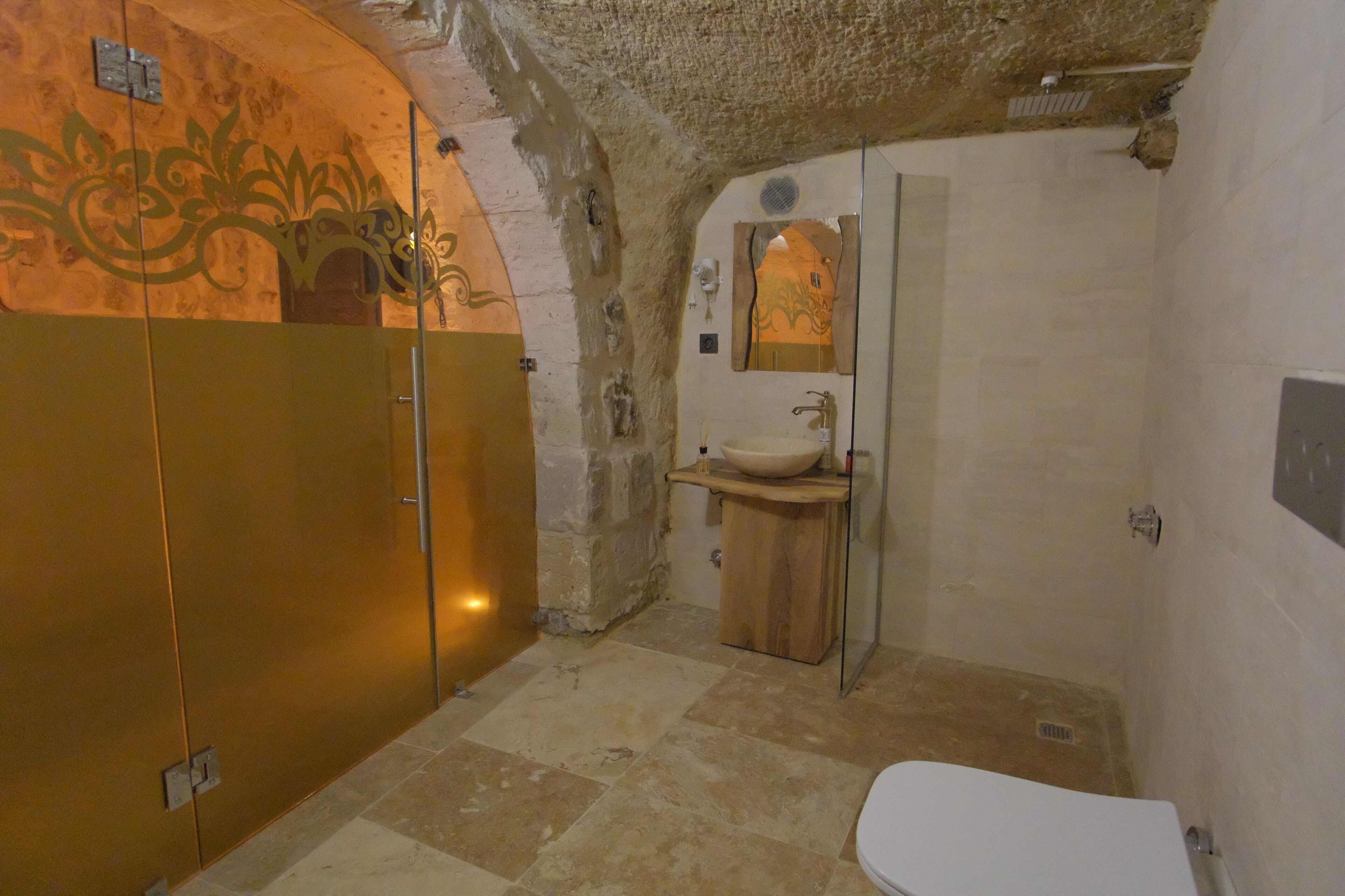 A bathroom with a stone wall, a wooden vanity, a white sink, and a mirror.