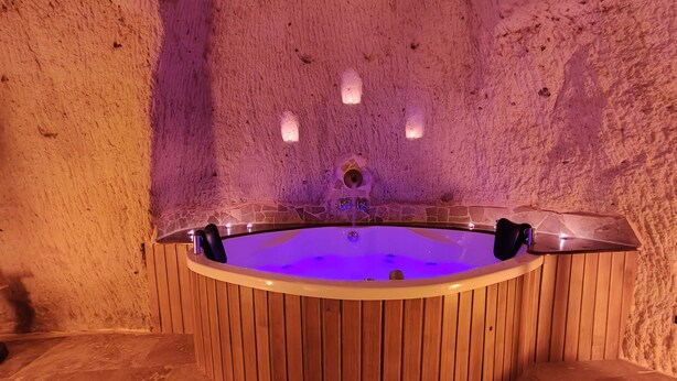 A hot tub in a rustic stone-walled room with wooden paneling. - Euphoria Cave House (Nevsehir)