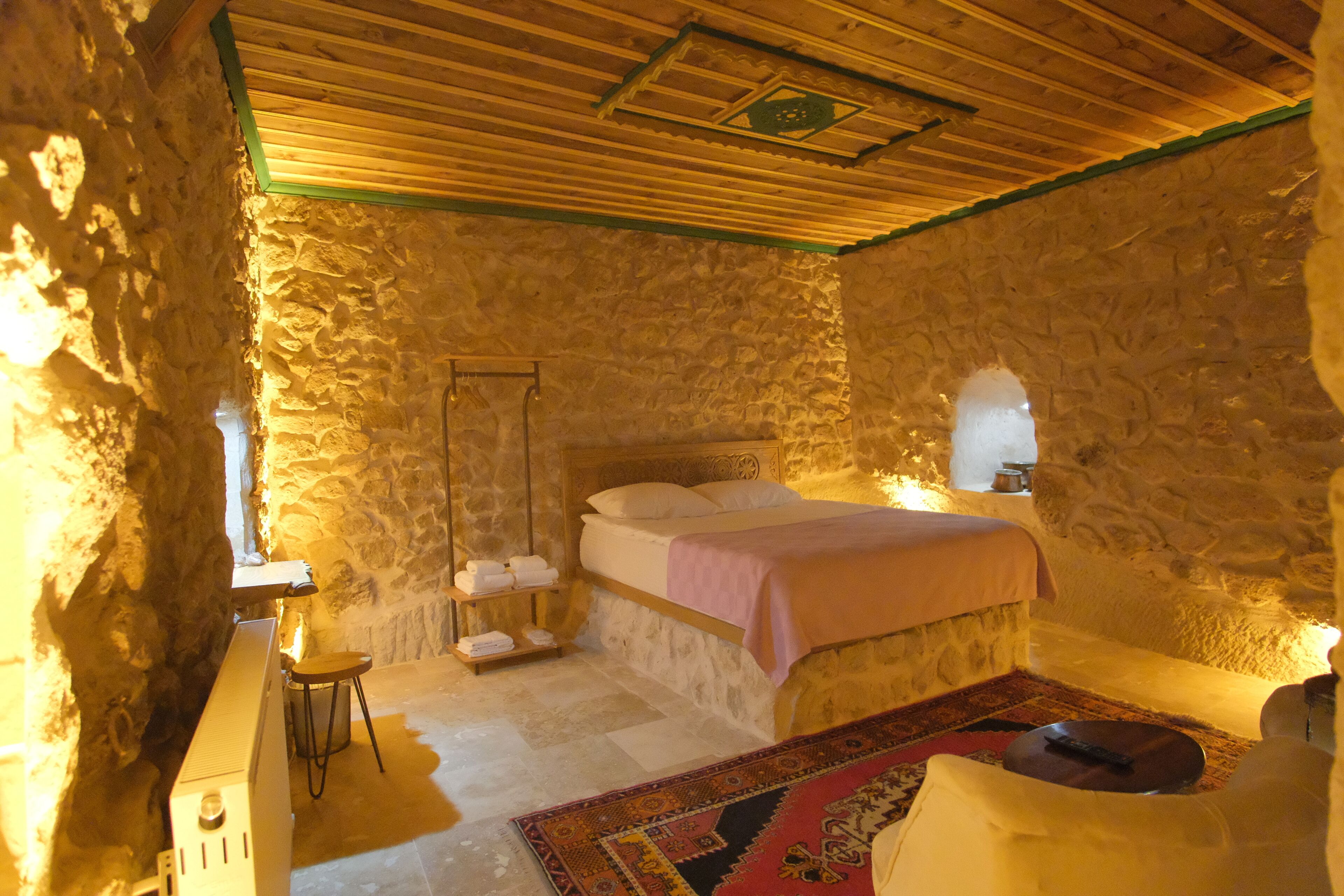 A stone-walled bedroom with a bed, a small stool, a nightstand, and a night lamp.
