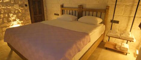 A single bed with a wooden headboard in a room with stone walls and a wooden door.