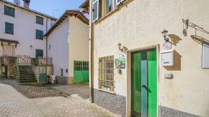Uma rua estreita com um edifício que tem uma porta verde e uma pequena janela com grade de metal.