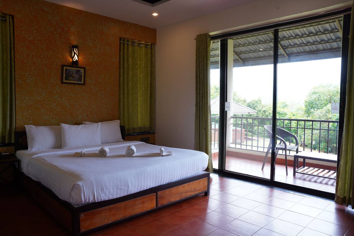 A hotel room with a large bed, a balcony with a chair, and a view of the outside.